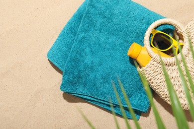Photo of Beach towel, straw bag, sunscreen product and sunglasses on sand outdoors, flat lay. Space for text