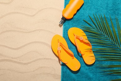 Photo of Beach towel, flip flops, sunscreen product and palm leaf on sand outdoors, flat lay. Space for text