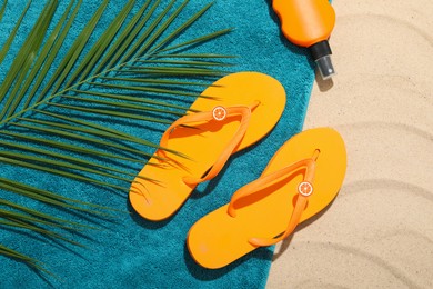 Photo of Beach towel, flip flops, sunscreen product and palm leaf on sand outdoors, flat lay