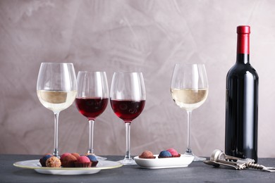 Photo of Delicious truffle bonbons and wine on black table against grey background