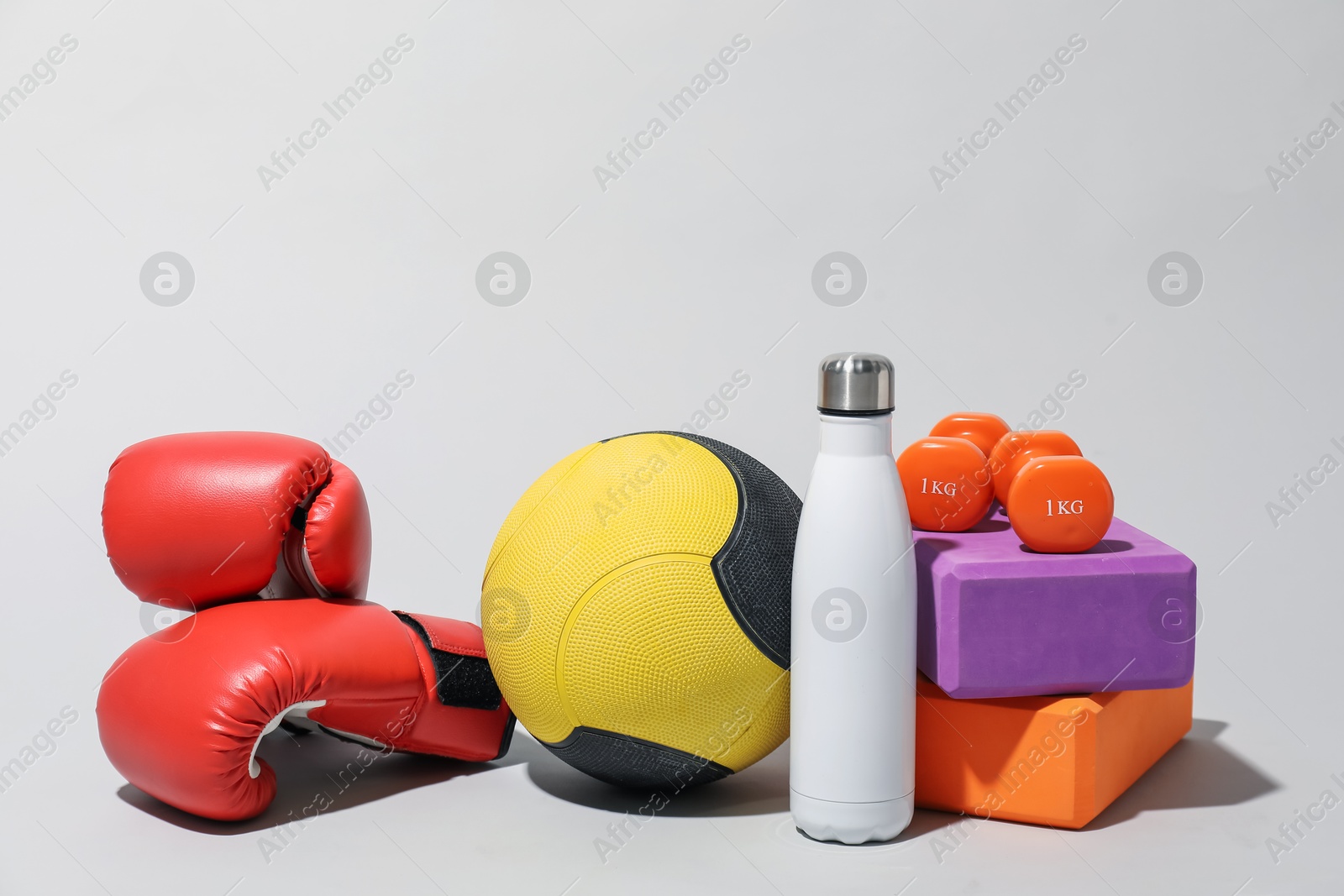 Medicine ball, boxing gloves, dumbbells, foam blocks and water bottle on light grey background Photo of Medicine ball, boxing gloves, dumbbells, foam blocks and water bottle on light grey background
