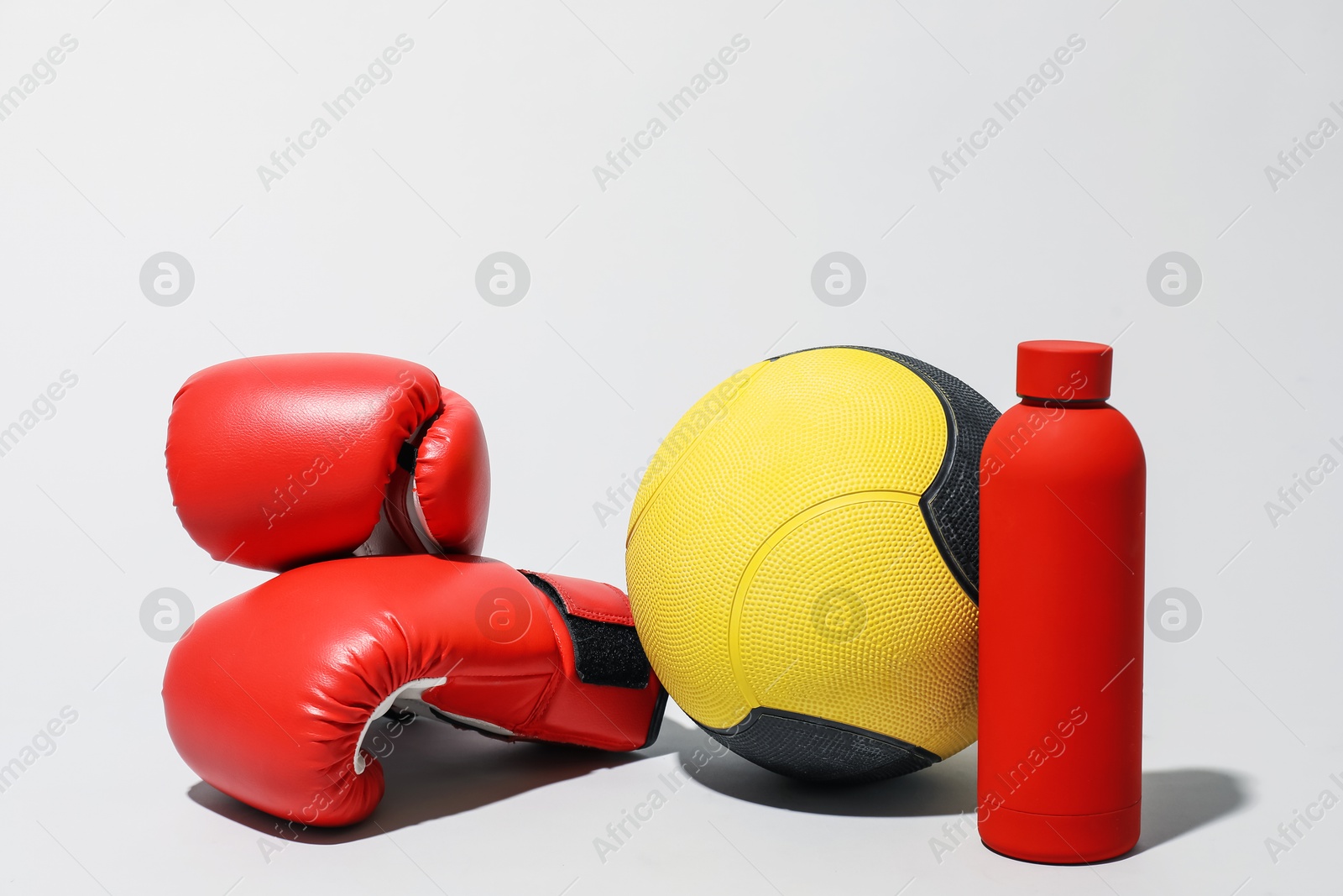 Medicine ball, boxing gloves and water bottle on light grey background Photo of Medicine ball, boxing gloves and water bottle on light grey background