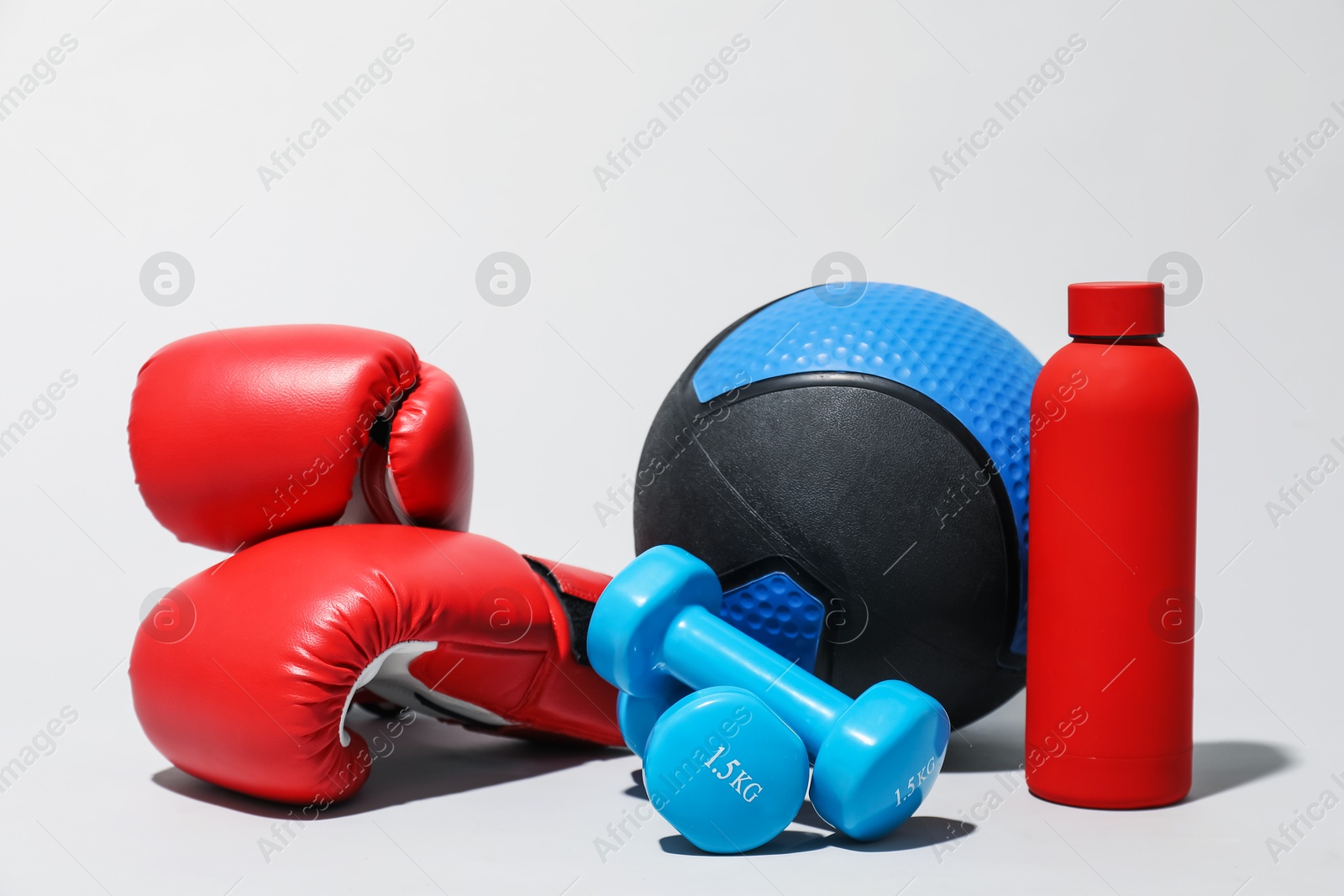 Medicine ball, boxing gloves, dumbbells and water bottle on light grey background Photo of Medicine ball, boxing gloves, dumbbells and water bottle on light grey background