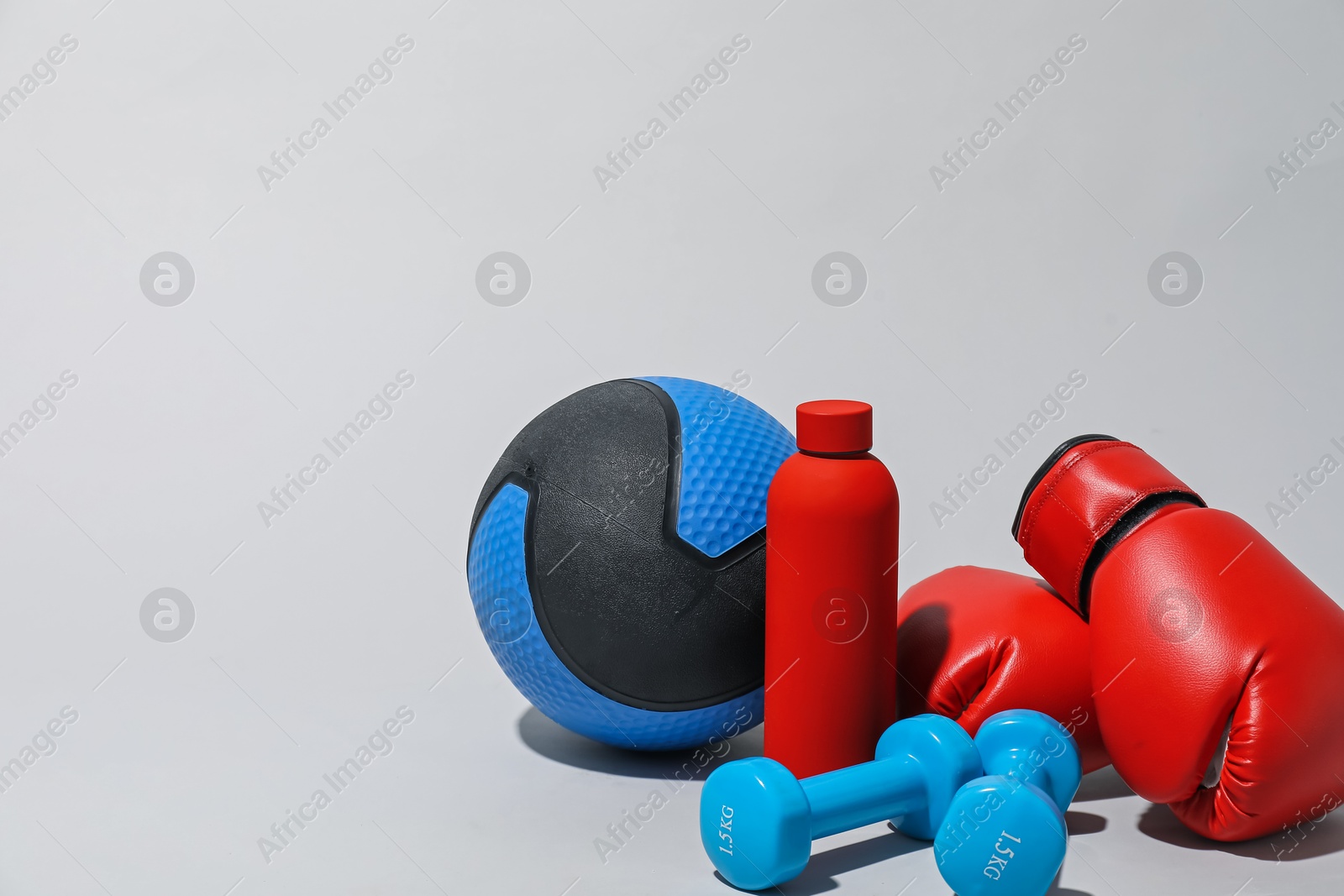 Medicine ball, boxing gloves, dumbbells and water bottle on light grey background, space for text Photo of Medicine ball, boxing gloves, dumbbells and water bottle on light grey background, space for text