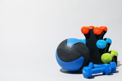 Photo of Medicine ball and dumbbells on light grey background, space for text