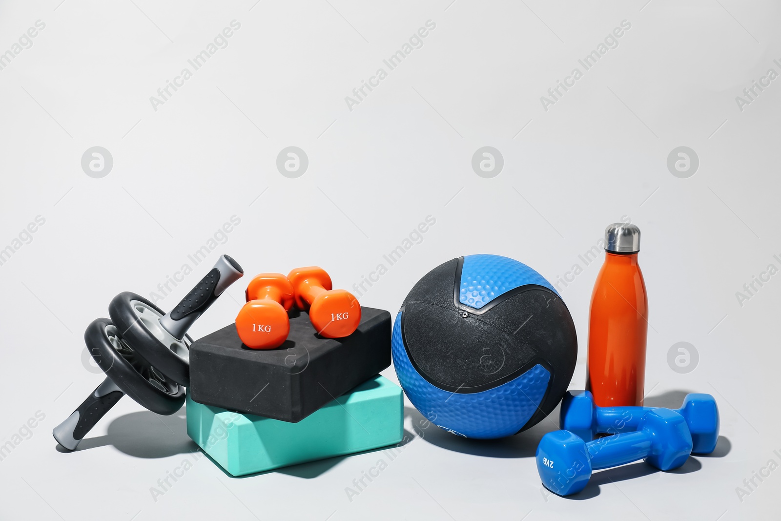 Medicine ball, dumbbells, water bottle, ab wheel and foam blocks on light grey background Photo of Medicine ball, dumbbells, water bottle, ab wheel and foam blocks on light grey background
