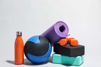 Photo of Medicine ball, dumbbells, water bottle, foam blocks and fitness mat on light grey background