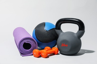 Photo of Medicine ball, dumbbells, kettlebell and fitness mat on light grey background