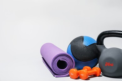 Photo of Medicine ball, dumbbells, kettlebell and fitness mat on light grey background. Space for text