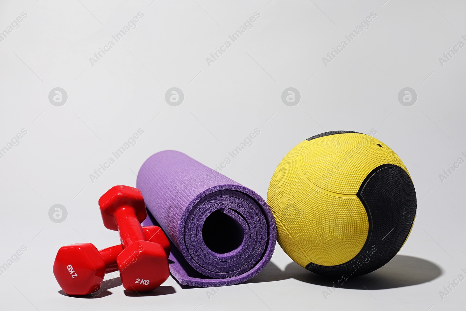Medicine ball, dumbbells and fitness mat on light grey background Photo of Medicine ball, dumbbells and fitness mat on light grey background