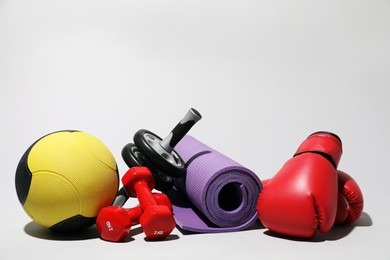 Photo of Medicine ball, dumbbells, ab wheel, boxing gloves and fitness mat on light grey background