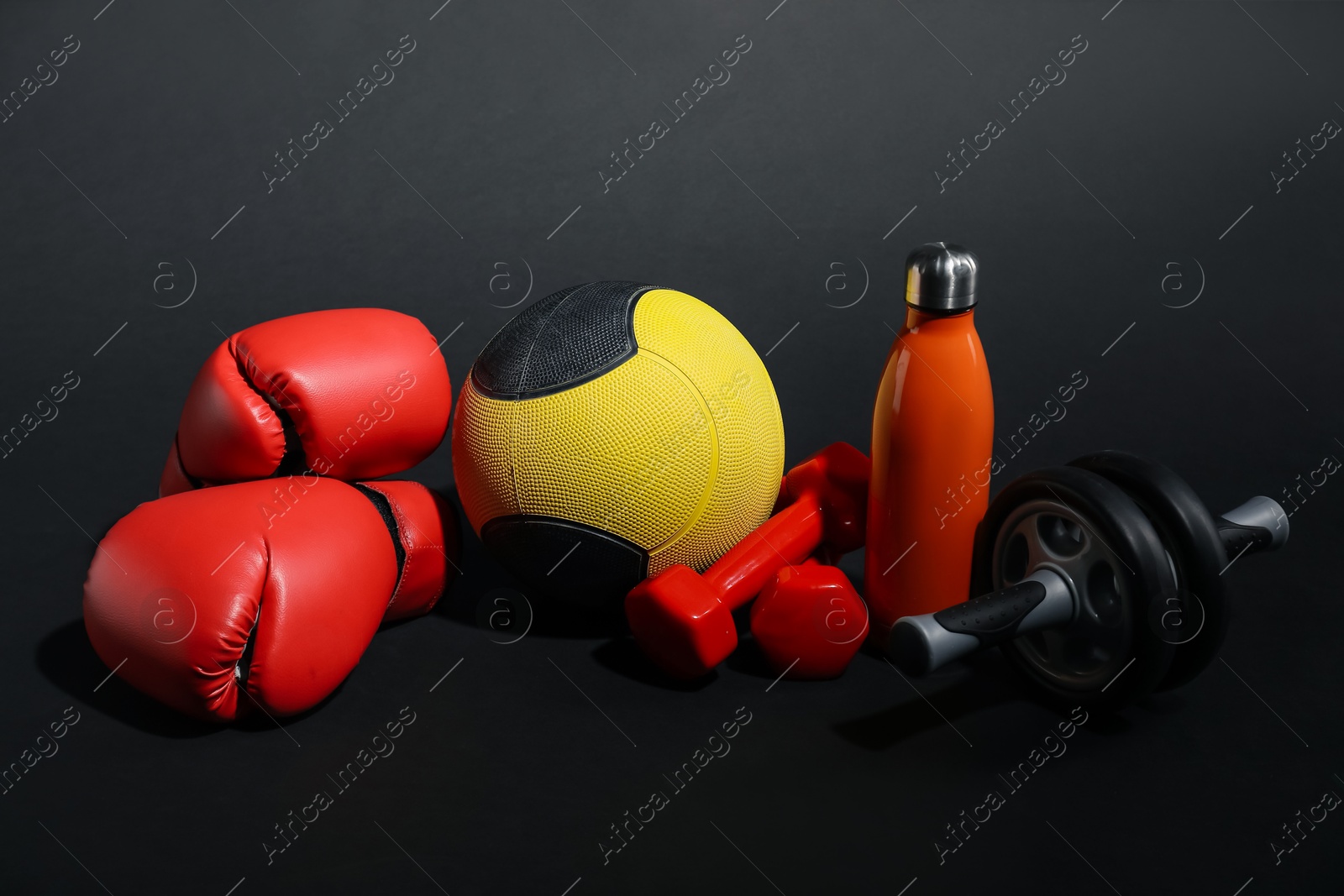 Medicine ball, dumbbells, ab wheel, water bottle and boxing gloves on black background Photo of Medicine ball, dumbbells, ab wheel, water bottle and boxing gloves on black background
