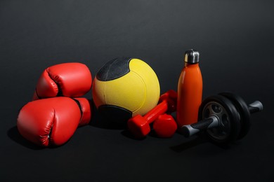 Photo of Medicine ball, dumbbells, ab wheel, water bottle and boxing gloves on black background
