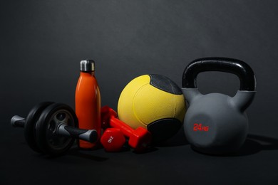 Photo of Medicine ball, dumbbells, ab wheel, water bottle and kettlebell on black background