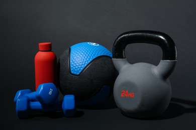 Photo of Medicine ball, dumbbells, kettlebell and water bottle on black background