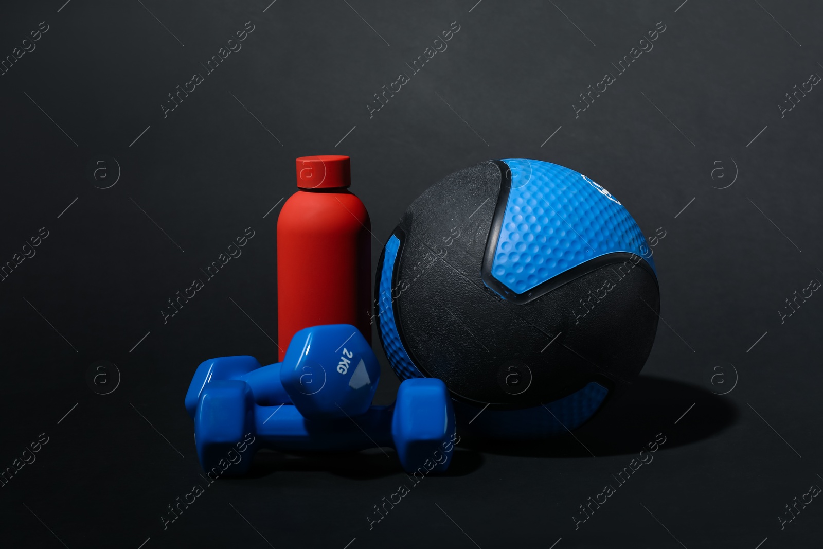 Medicine ball, dumbbells and water bottle on black background Photo of Medicine ball, dumbbells and water bottle on black background