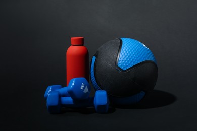 Photo of Medicine ball, dumbbells and water bottle on black background