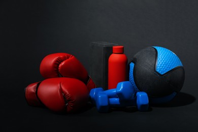 Photo of Medicine ball, dumbbells, boxing gloves, foam block and water bottle on black background
