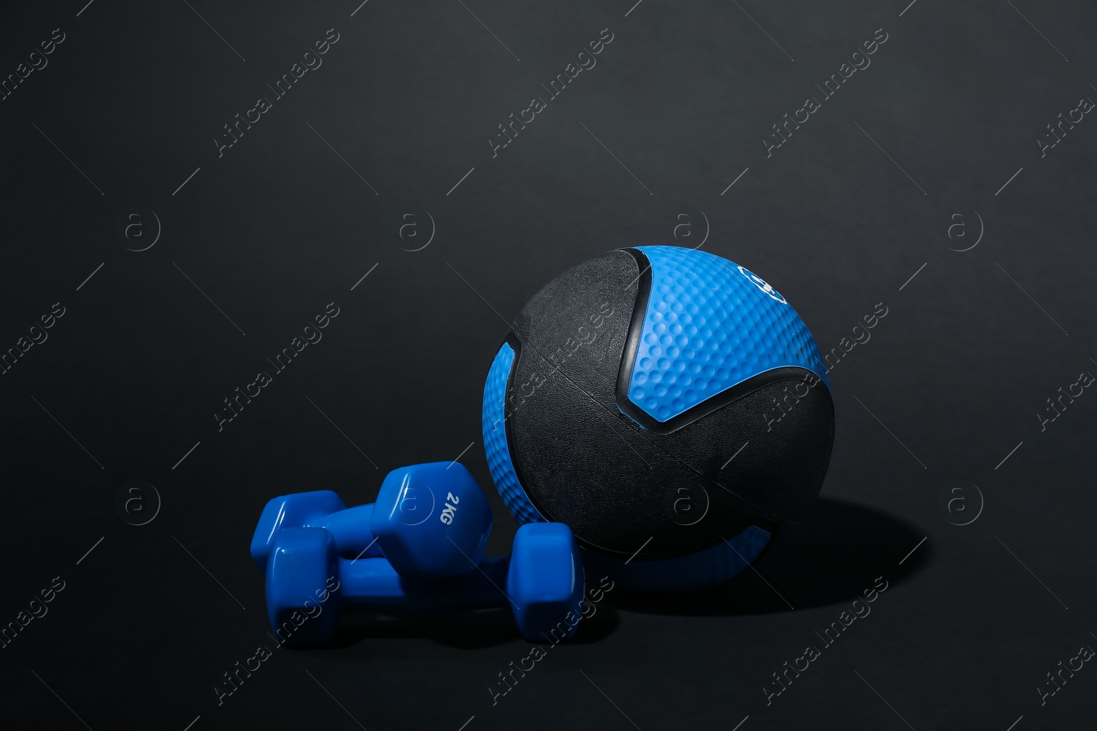 Medicine ball and dumbbells on black background Photo of Medicine ball and dumbbells on black background