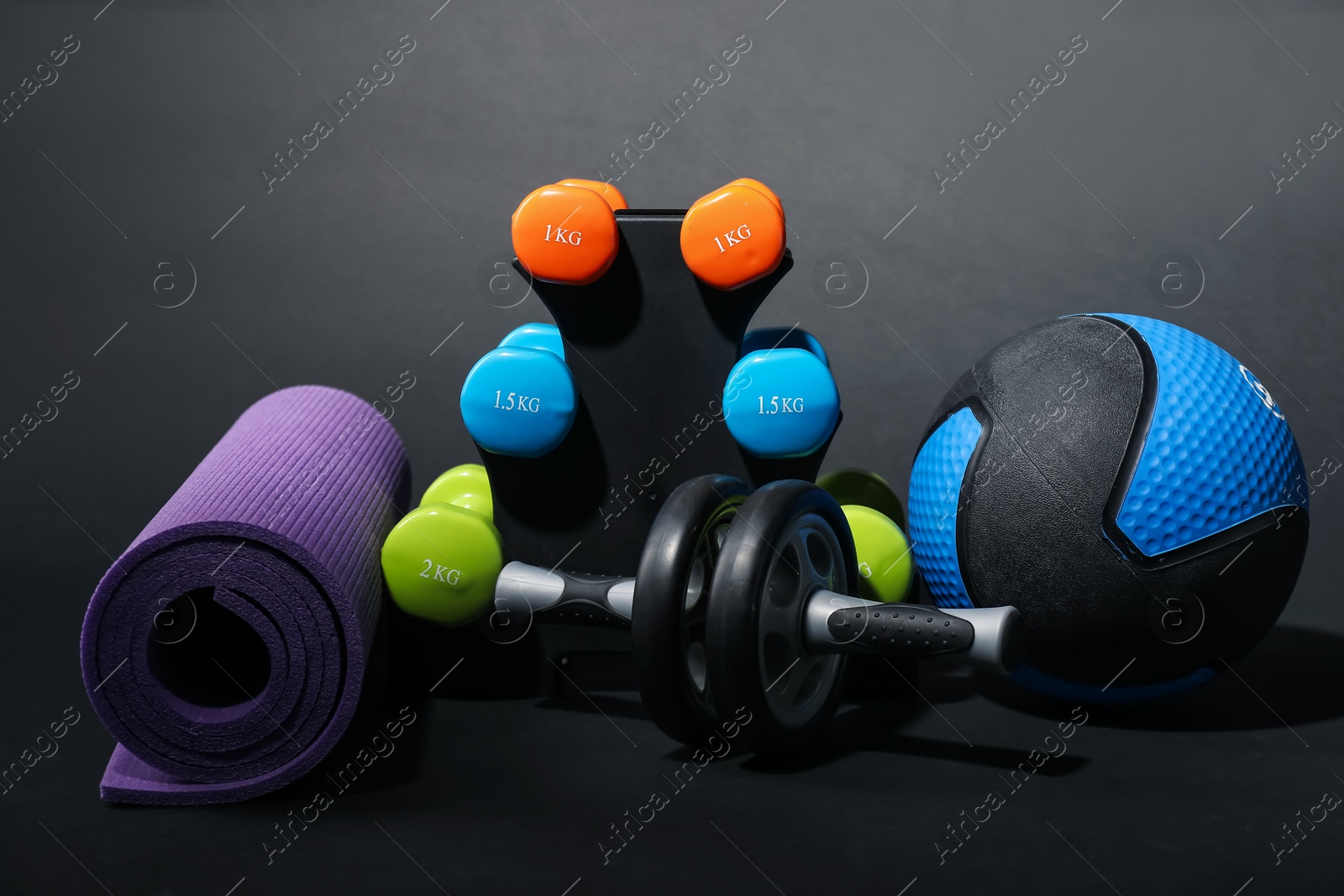 Photo of Medicine ball, dumbbells, fitness mat and ab wheel on black background
