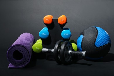 Photo of Medicine ball, dumbbells, fitness mat and ab wheel on black background
