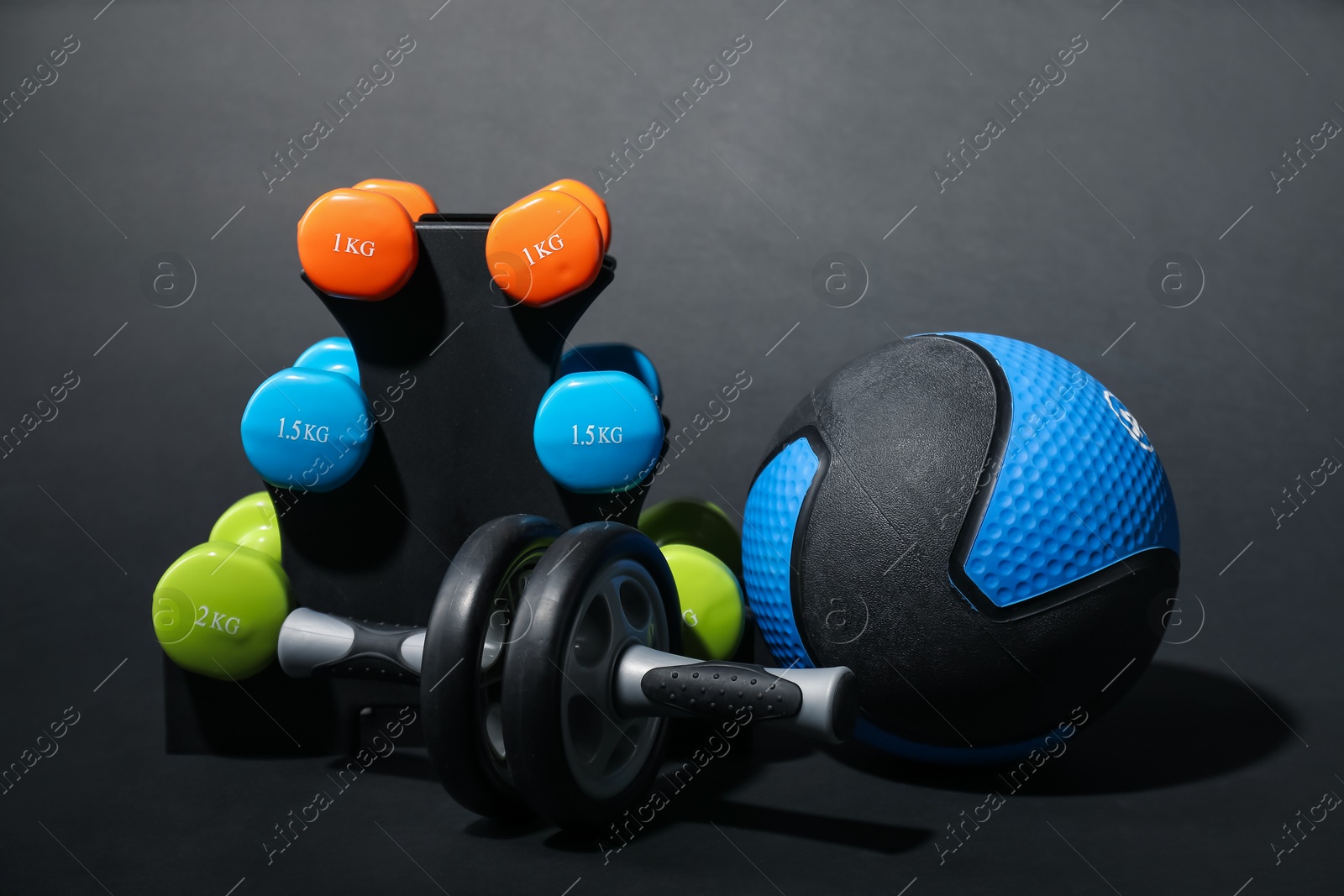 Medicine ball, dumbbells and ab wheel on black background Photo of Medicine ball, dumbbells and ab wheel on black background