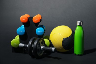 Photo of Medicine ball, dumbbells, ab wheel and water bottle on black background