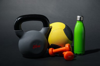Photo of Medicine ball, dumbbells, water bottle and kettlebell on black background