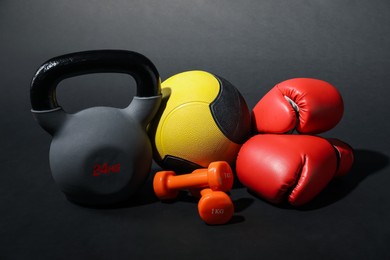 Photo of Medicine ball, dumbbells, boxing gloves and kettlebell on black background