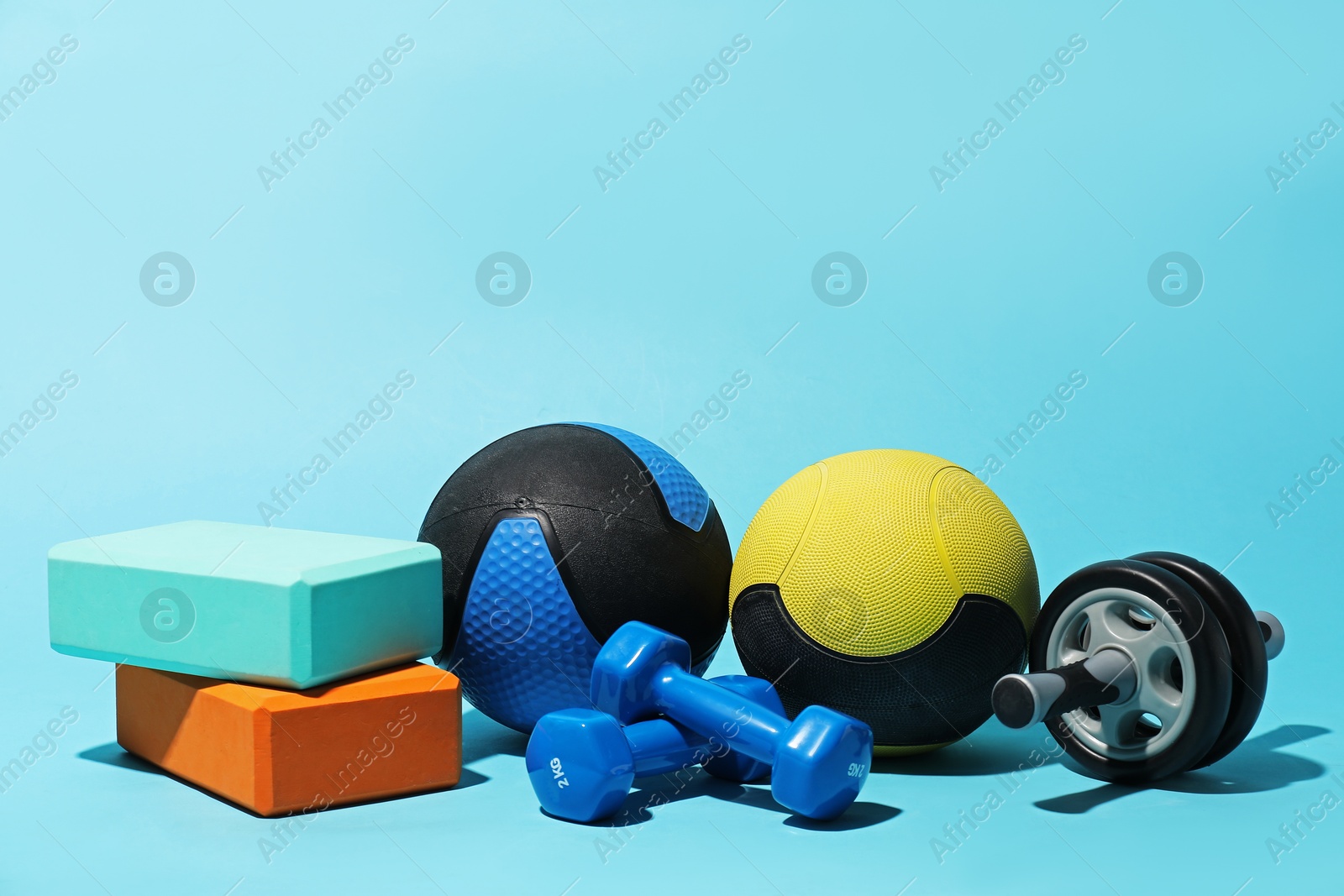 Medicine balls, foam blocks, ab wheel and dumbbells on light blue background Photo of Medicine balls, foam blocks, ab wheel and dumbbells on light blue background