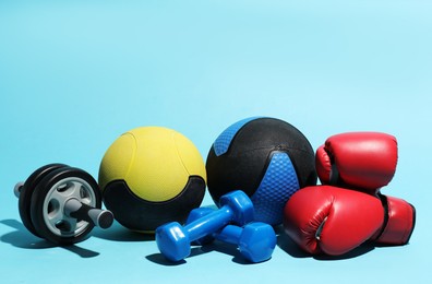 Photo of Medicine balls, boxing gloves, ab wheel and dumbbells on light blue background