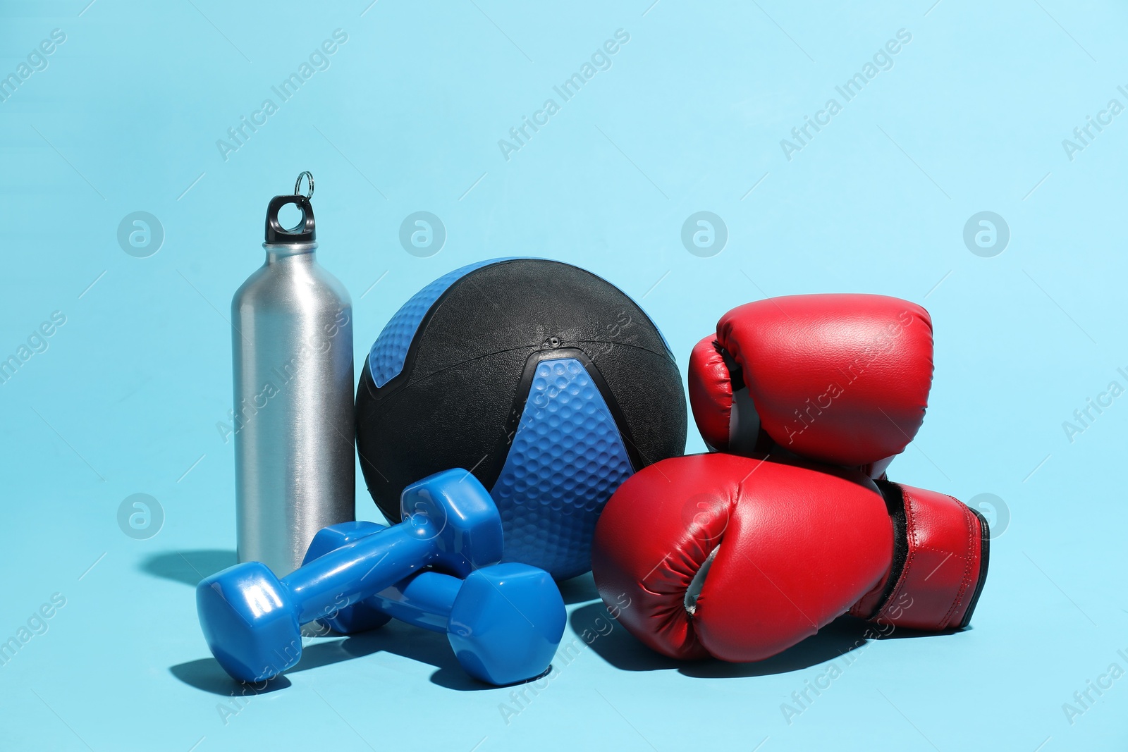 Medicine ball, boxing gloves, kettlebell, water bottle and dumbbells on light blue background Photo of Medicine ball, boxing gloves, kettlebell, water bottle and dumbbells on light blue background
