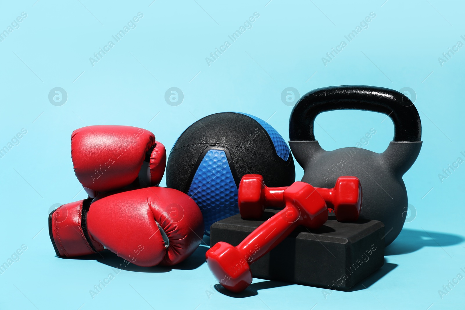 Medicine ball, boxing gloves, foam block, kettlebell and dumbbells on light blue background Photo of Medicine ball, boxing gloves, foam block, kettlebell and dumbbells on light blue background