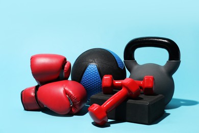 Photo of Medicine ball, boxing gloves, foam block, kettlebell and dumbbells on light blue background