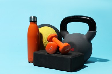 Photo of Medicine ball, kettlebell, water bottle, foam block and dumbbells on light blue background
