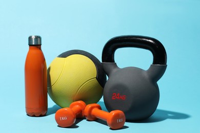 Photo of Medicine ball, kettlebell, water bottle and dumbbells on light blue background