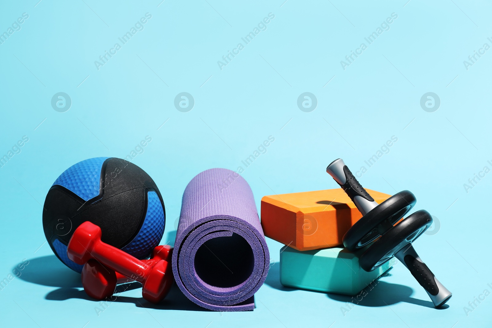 Medicine ball, ab wheel, foam blocks, fitness mat and dumbbells on light blue background Photo of Medicine ball, ab wheel, foam blocks, fitness mat and dumbbells on light blue background
