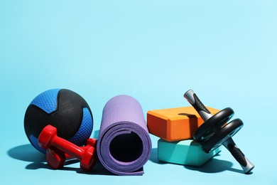 Photo of Medicine ball, ab wheel, foam blocks, fitness mat and dumbbells on light blue background