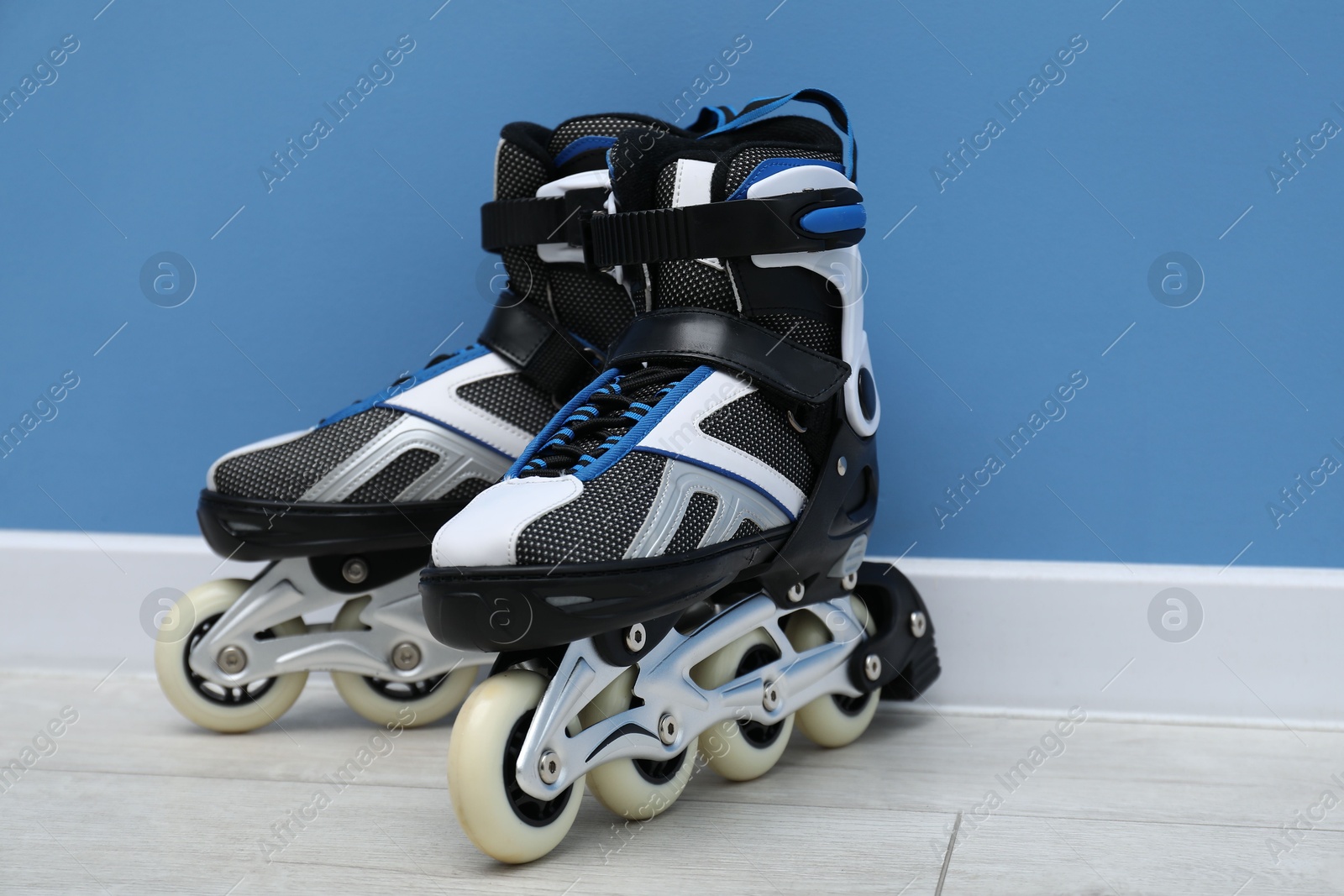 Pair of roller skates on floor near light blue wall Photo of Pair of roller skates on floor near light blue wall