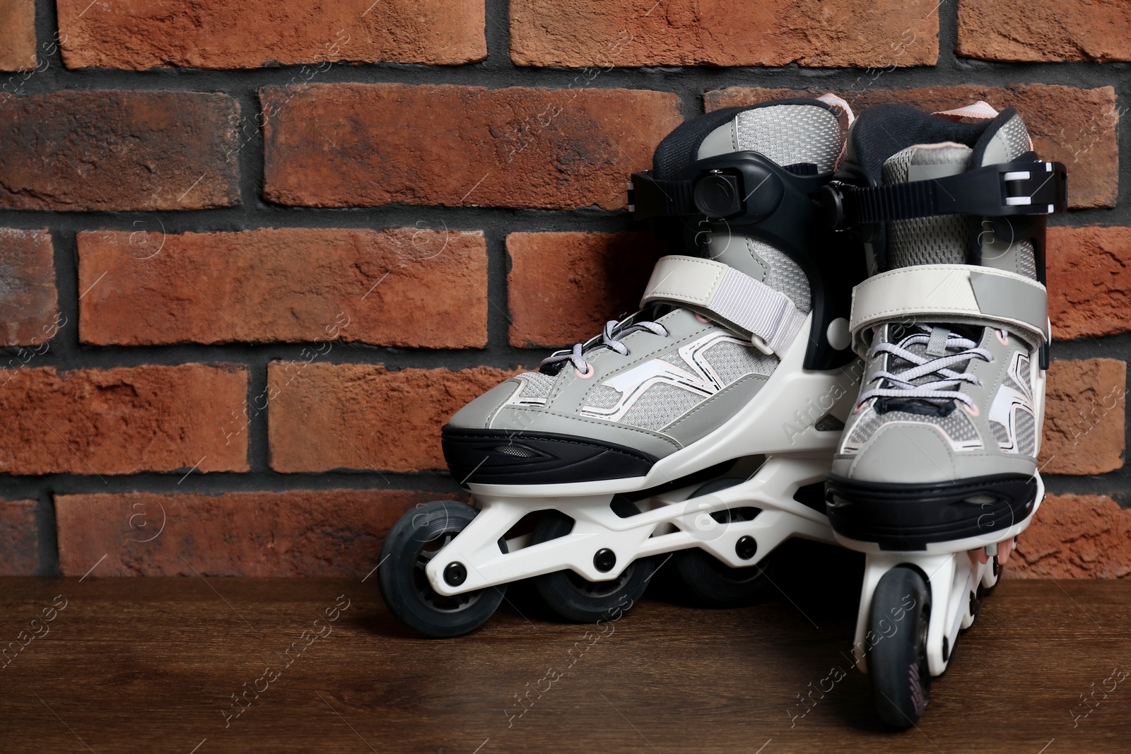 Pair of roller skates on wooden table near brick wall, space for text Photo of Pair of roller skates on wooden table near brick wall, space for text