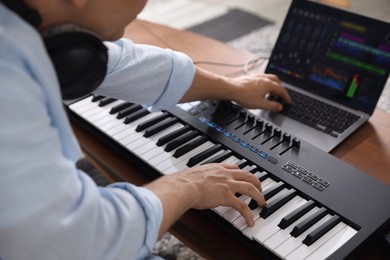 Photo of Man working with MIDI keyboard and laptop at table indoors, selective focus