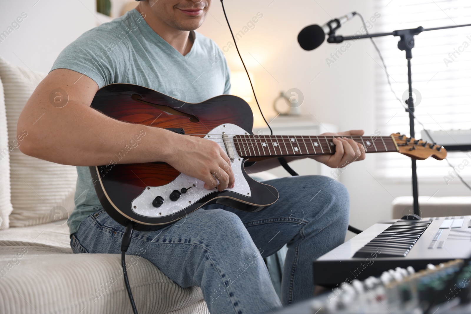 Man working with guitar and MIDI keyboard on sofa in home studio, closeup Photo of Man working with guitar and MIDI keyboard on sofa in home studio, closeup