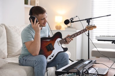 Photo of Man in headphones working with guitar and MIDI keyboard on sofa in home studio