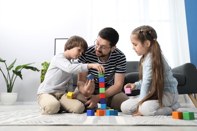 Photo of Father and his children playing with colorful cubes on floor at home