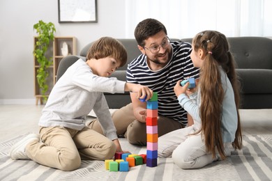 Photo of Father and his children playing with colorful cubes on floor at home
