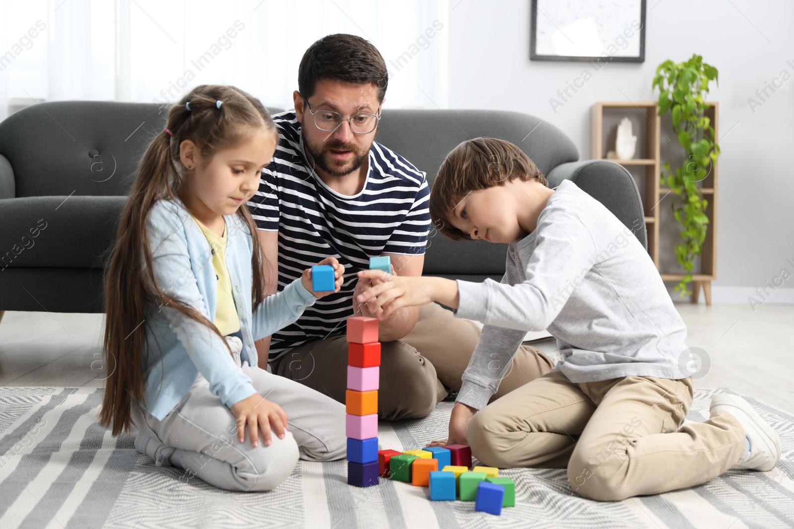 Father and his children playing with colorful cubes on floor at home Photo of Father and his children playing with colorful cubes on floor at home