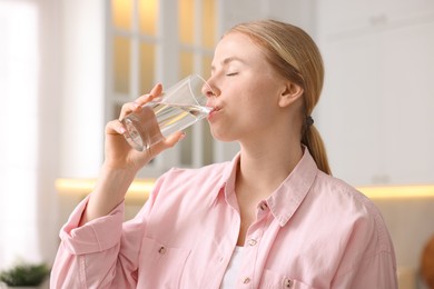 Photo of Young woman drinking water from glass in kitchen