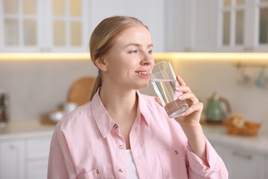 Photo of Young woman drinking water from glass in kitchen