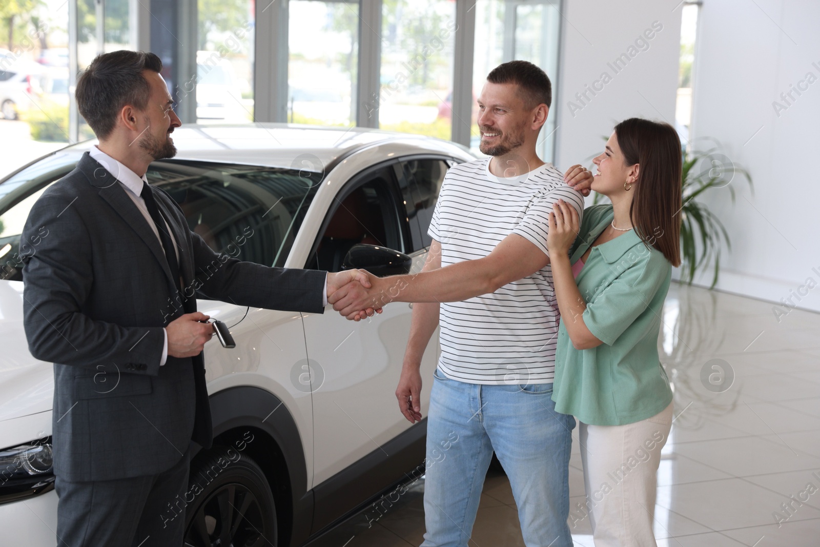Salesman shaking hands with happy family near new car in salon Photo of Salesman shaking hands with happy family near new car in salon