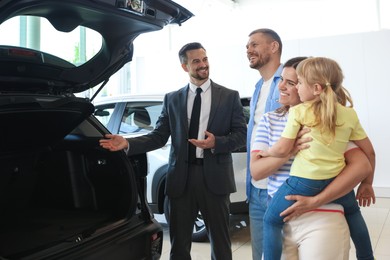 Photo of Salesman showing new car to happy family in salon
